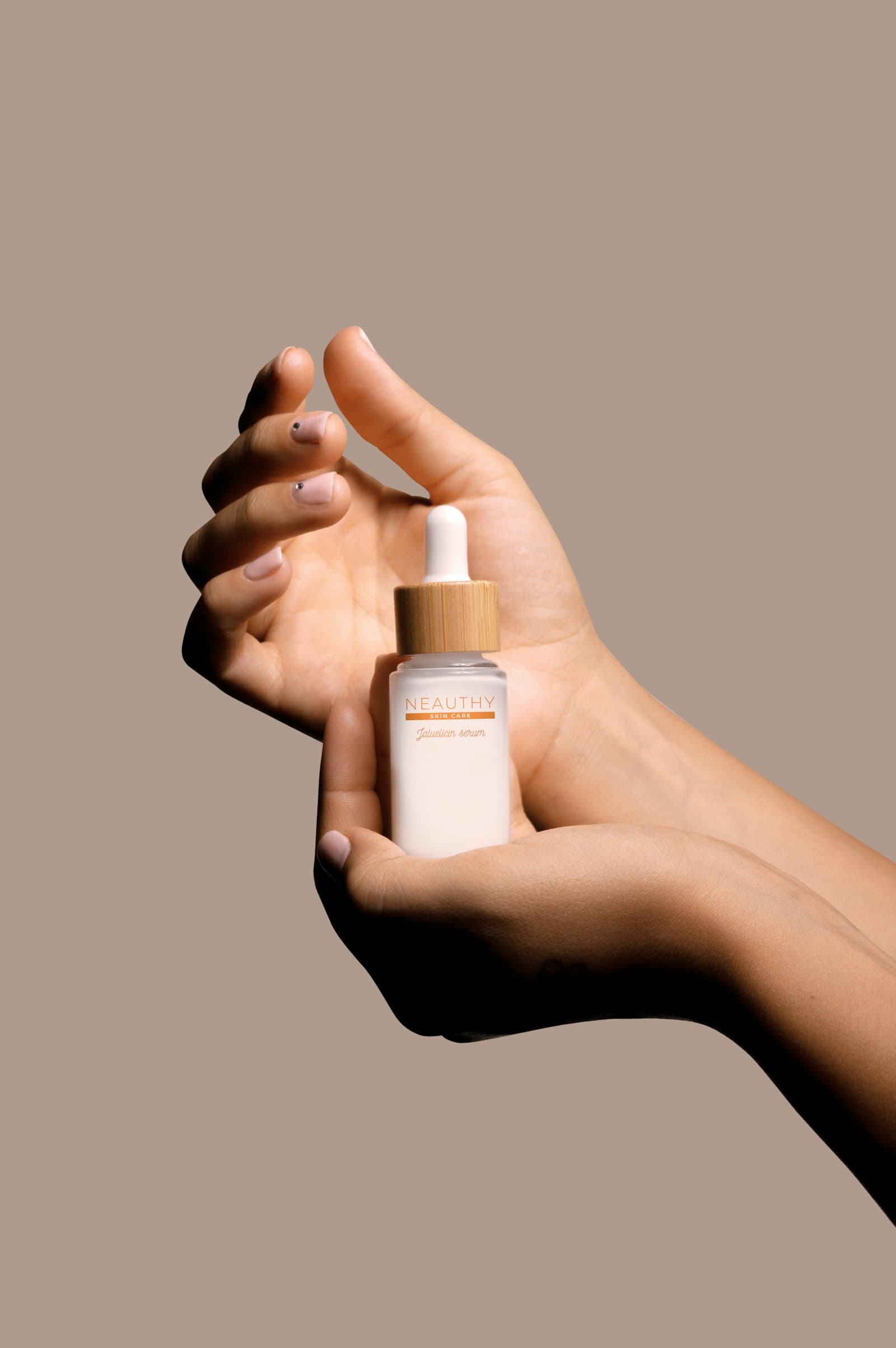 A hand holding a small bottle of serum against a beige wall